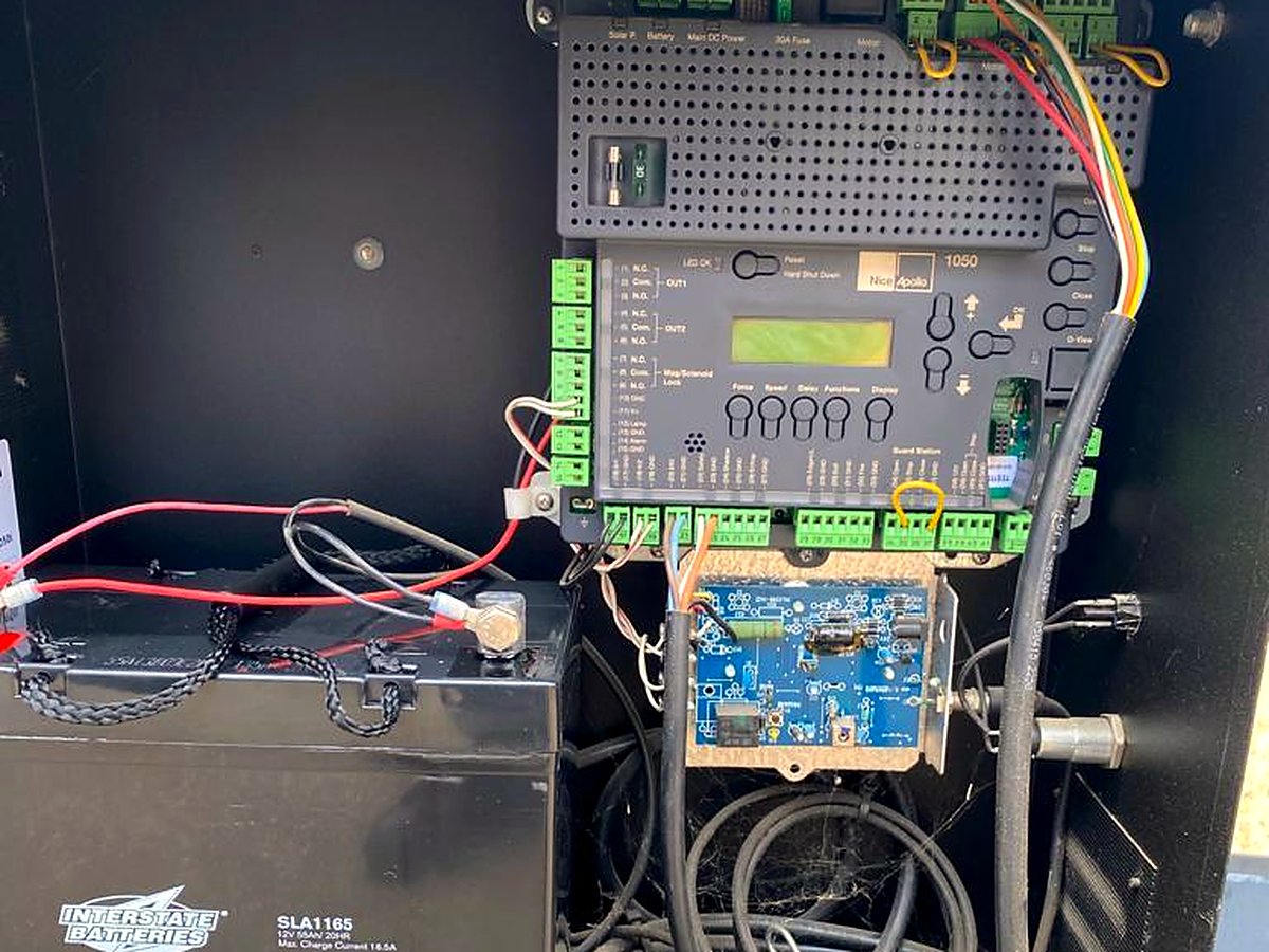 Inside an automatic gate operator cabinet showing the control board and battery backup